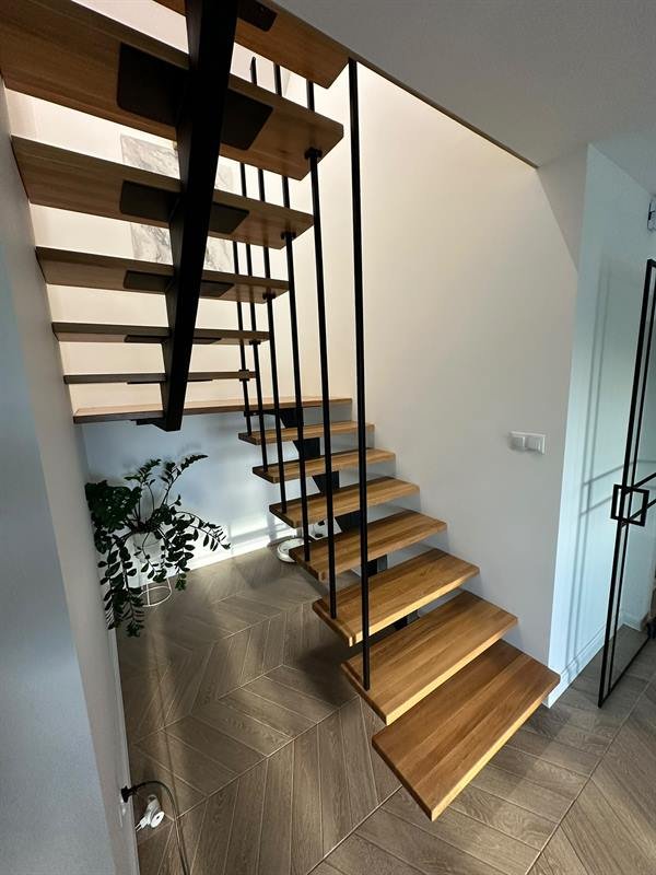 Drewniane stopnie na czarnej stalowej konstrukcji ze smukłą balustradą